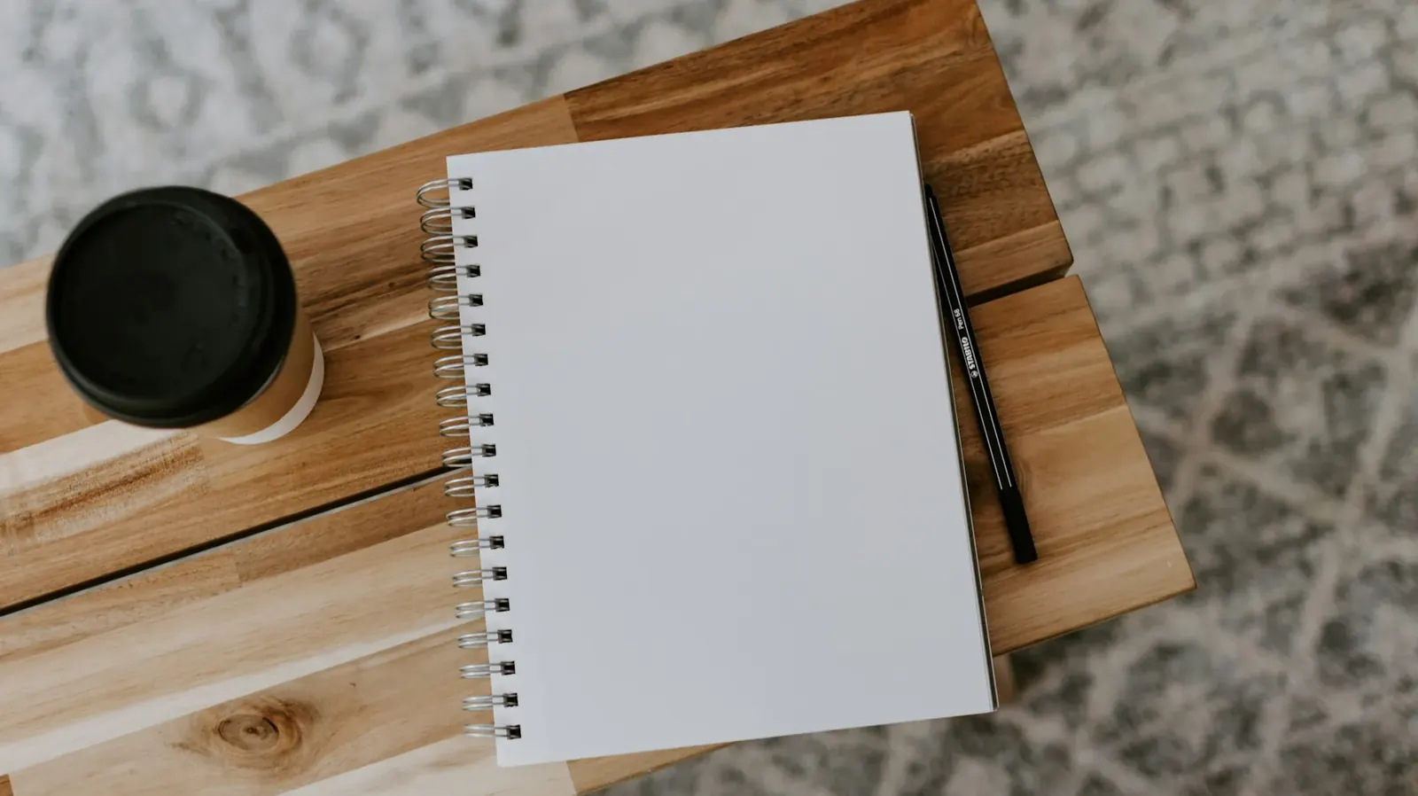 Open notebook with a pen and coffee on a wooden table