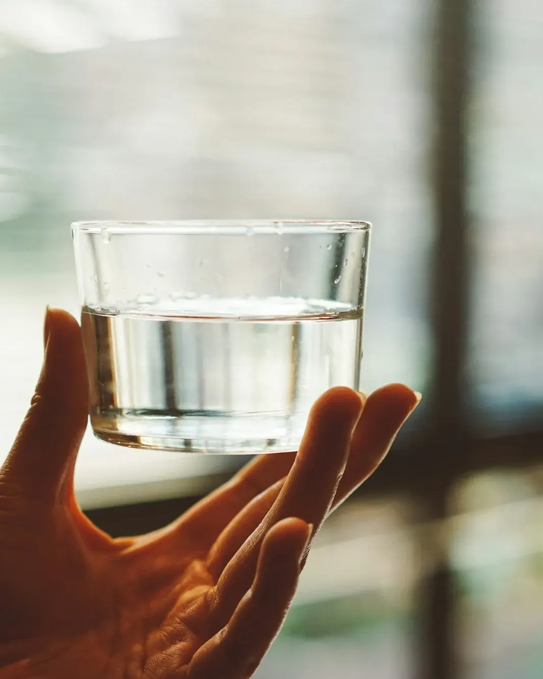 Hand holding a glass of clear water against window light