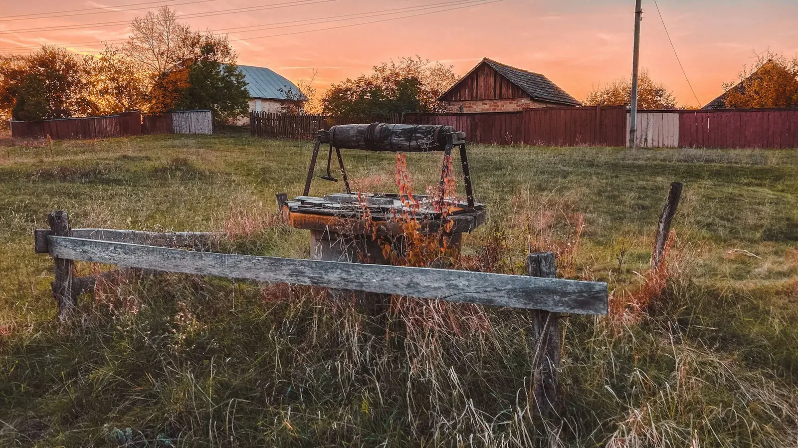 Old well frame in a grassy field at sunset